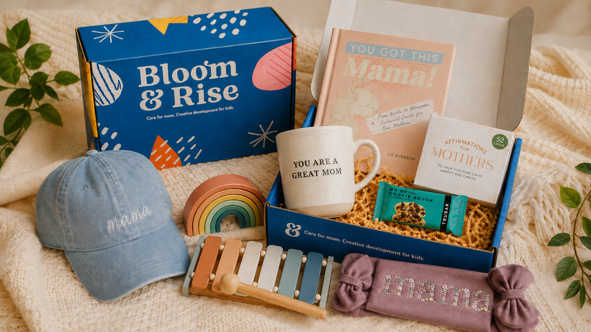 A curated gift box set for moms on a cozy beige blanket, featuring a blue 'Bloom & Rise' box, a white mug reading 'YOU ARE A GREAT MOM', a pastel rainbow toy, a lavender 'MAMA' pillow, a light blue baseball cap, and a wooden xylophone.